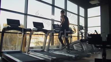 年轻的运动男女在运动健身房的跑步机上锻炼和跑步。 在大的全景窗户附近